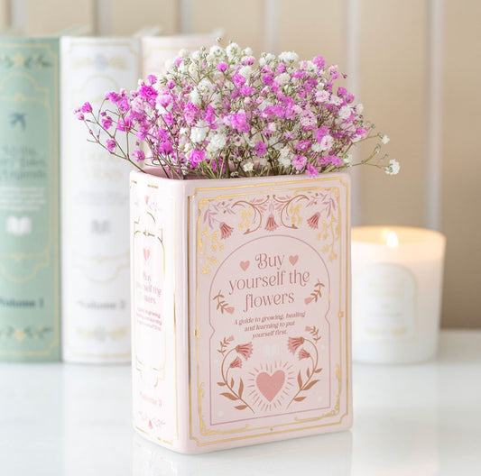 Pink book shaped vase. Baby pink colour with pink writing and delicate details. Book is standing upright with flowers inserted from where the top pages would be. Part of the book lover gift range.